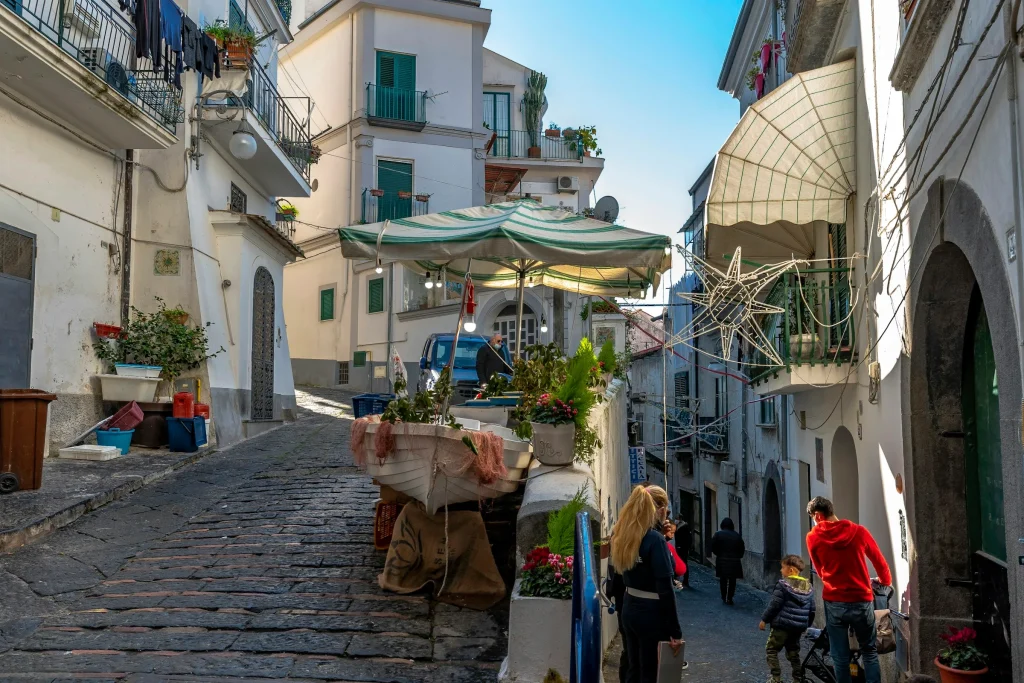 A narrow village street on the coast with awnings and a market stall