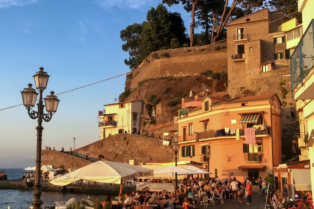 People walking past the buildings of the Sorrento marina in the evening light